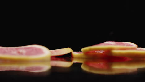 Slow-motion.-Sliced-​​grapefruit-rings-falling-with-splashes-of-water-on-the-glass-on-a-dark-background.-Cut-into-slices